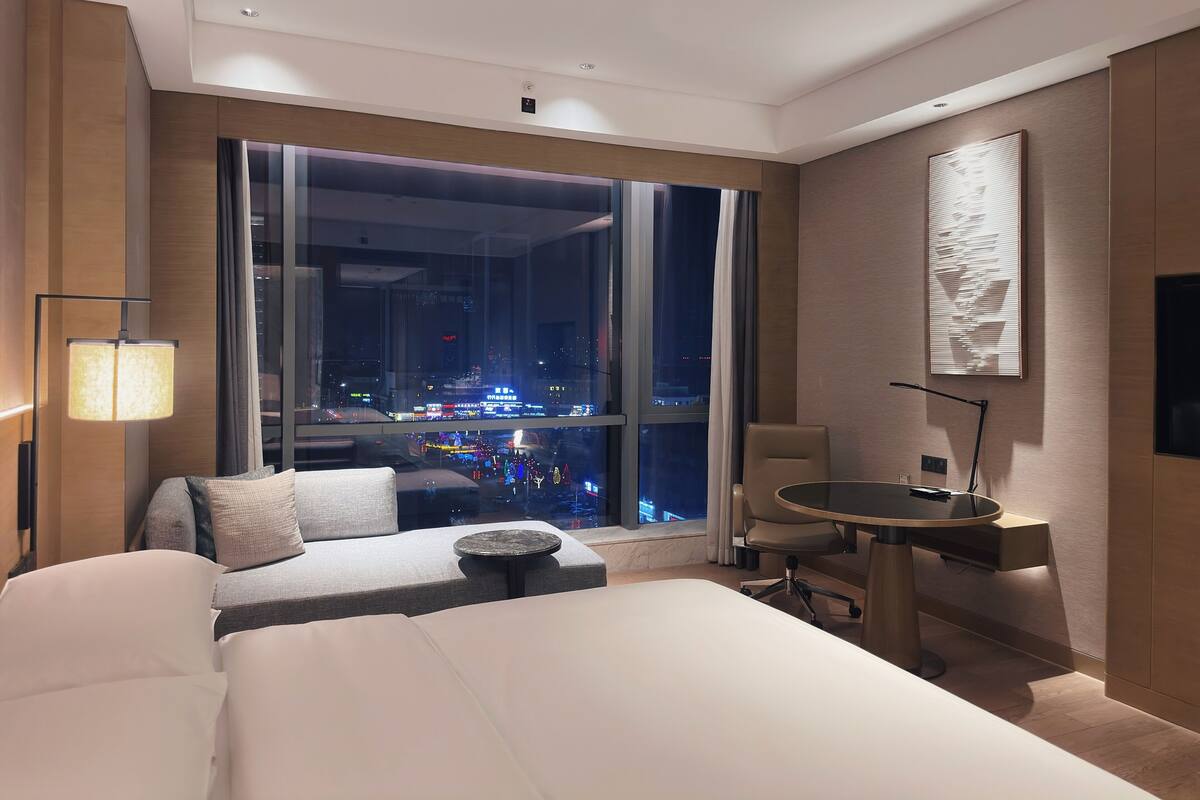 Una habitación de hotel con un ventanal grande, una cama, un escritorio y una silla.