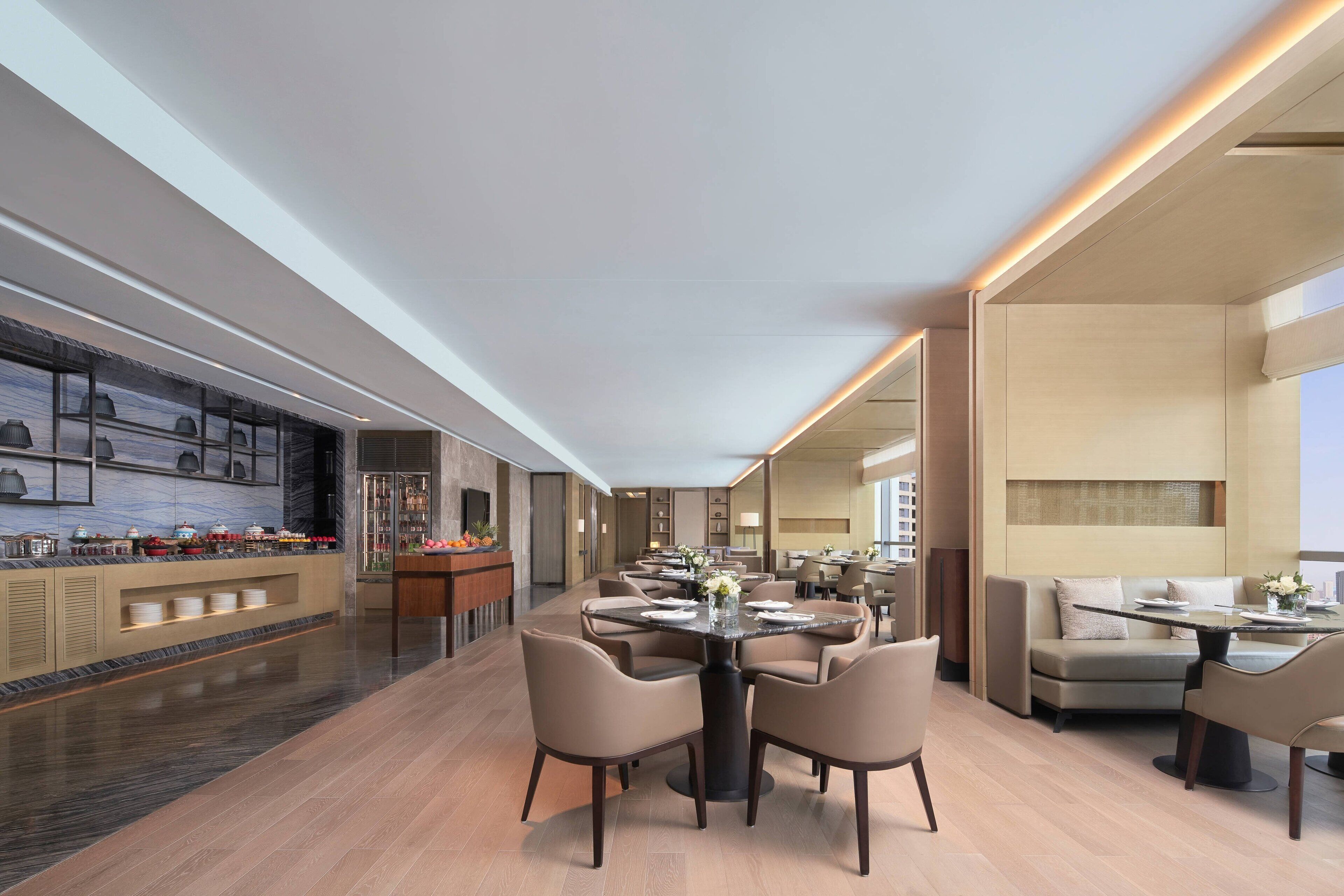 Een moderne hotellobby met een lange receptiebalie, verschillende zithoeken en een groot raam met uitzicht op de stad.