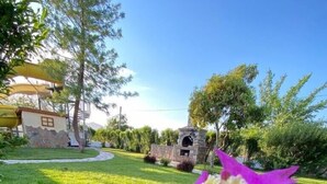 A garden with a stone structure, possibly a barbecue area, surrounded by lush greenery and a clear sky. - VILLA ZEZE 7 ROOMS 14 SLEEPS PRIVATE WATERSLIDES (Dalyan)