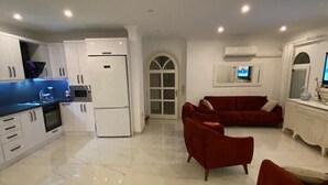 A modern kitchen with white cabinets and a marble floor. There is a red sofa set in the living area, and a TV mounted on the wall. - VILLA ZEZE 7 ROOMS 14 SLEEPS PRIVATE WATERSLIDES (Dalyan)