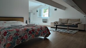 A bedroom with a bed, a sofa, and a window.