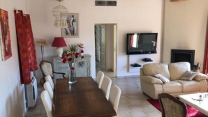 A dining area with a wooden table and chairs, a sofa, a TV, and a fireplace.