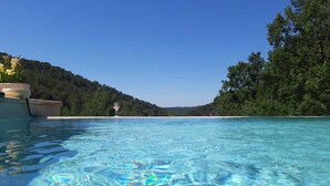 A clear pool with a view of a beach and forested hills.