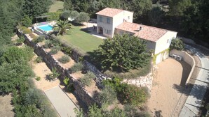 A two-story house with a swimming pool, surrounded by a stone wall and greenery.
