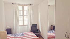 Une chambre avec deux lits, une chaise, une table de chevet, une lampe et une armoire.