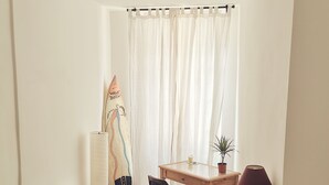 Une petite pièce bien éclairée, avec un lit, un bureau, une chaise, une lampe et une planche de surf.