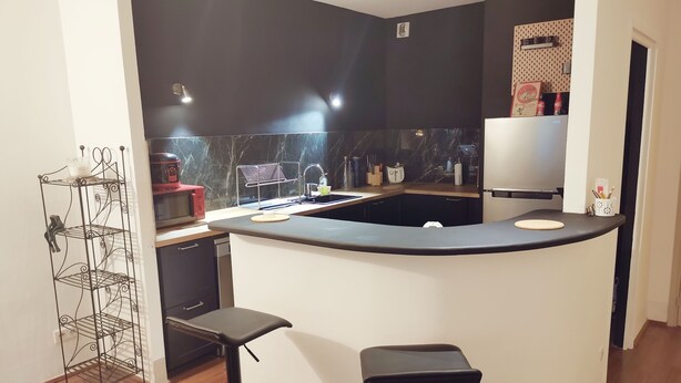 Une cuisine moderne avec un plan de travail noir, deux tabourets de bar, une machine à café et un évier.