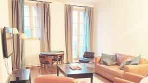 Un salon comprenant un canapé, des fauteuils, une table basse, un téléviseur et un coin repas avec une table et des chaises.