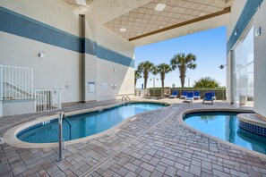 A pool area with two pools, a covered seating area, and palm trees in the background.