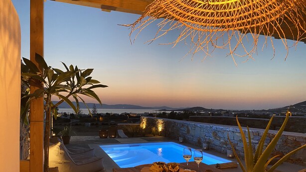 Una terraza con piscina, asientos y vista al mar al anochecer.