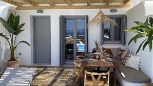 Un patio soleado con mesa de madera dispuesta para comer, zona de estar con cojines y plantas en macetas.