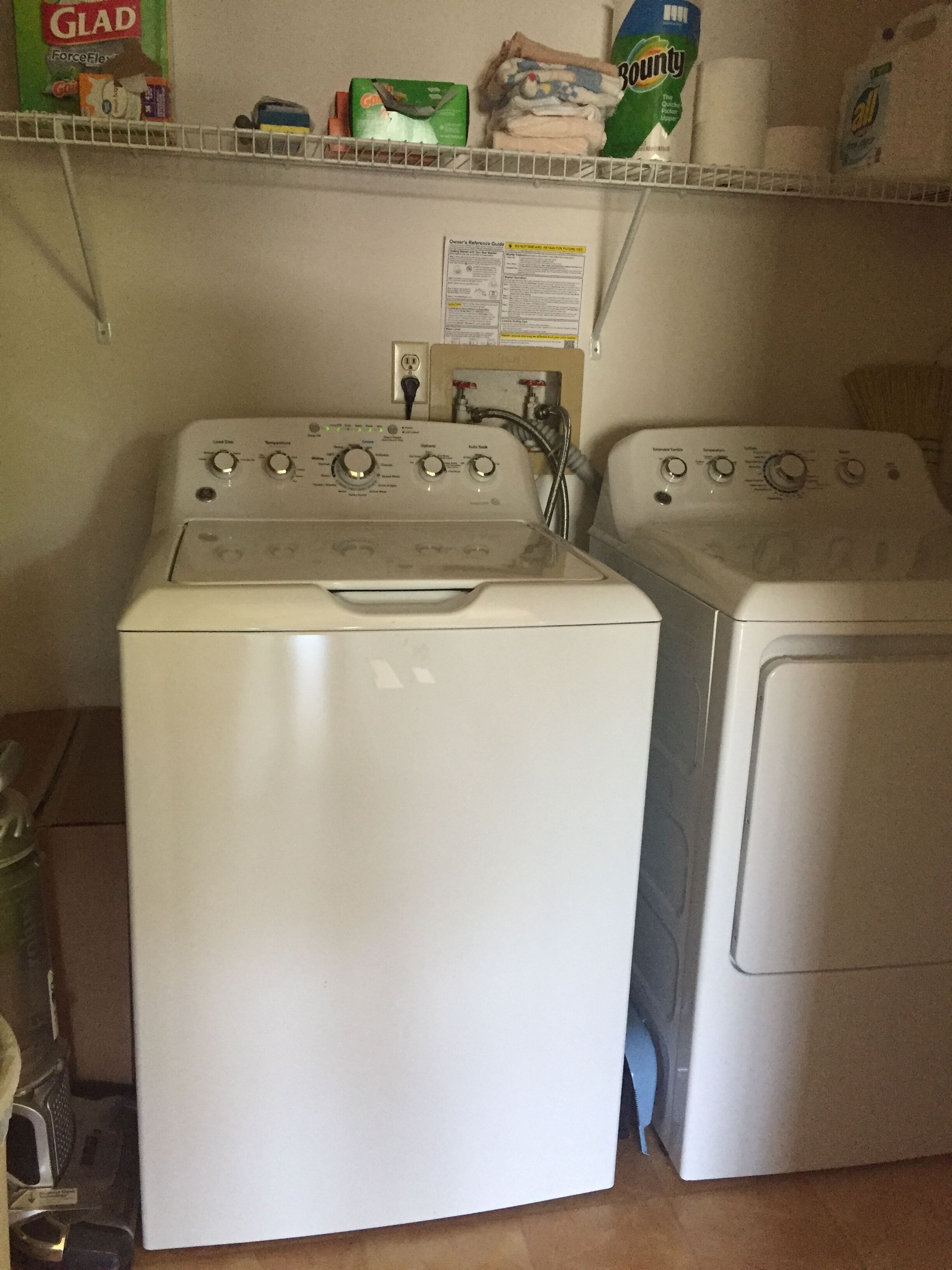 A laundry area with two front-loading washing machines and a shelf above containing cleaning supplies.