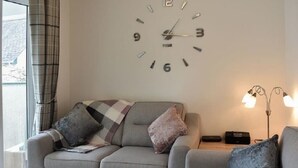 A modern living room with a grey sofa, a wall clock, and a floor lamp. - Claife View - Parking, Balcony, 1 min walk to central Bowness (Bowness-on-Windermere)