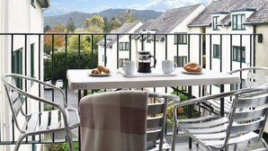 A balcony with a table set for breakfast, chairs, and a view of buildings and hills. - Claife View - Parking, Balcony, 1 min walk to central Bowness (Bowness-on-Windermere)