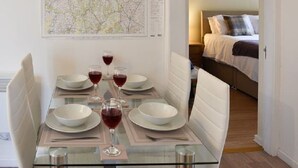 A dining area with a glass table set for four, a map on the wall, and a bedroom in the background. - Claife View - Parking, Balcony, 1 min walk to central Bowness (Bowness-on-Windermere)