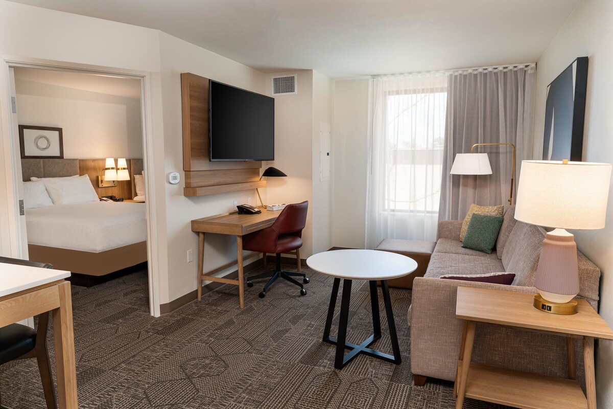 A hotel room with a bed, desk, chair, sofa, and a TV mounted on the wall.
