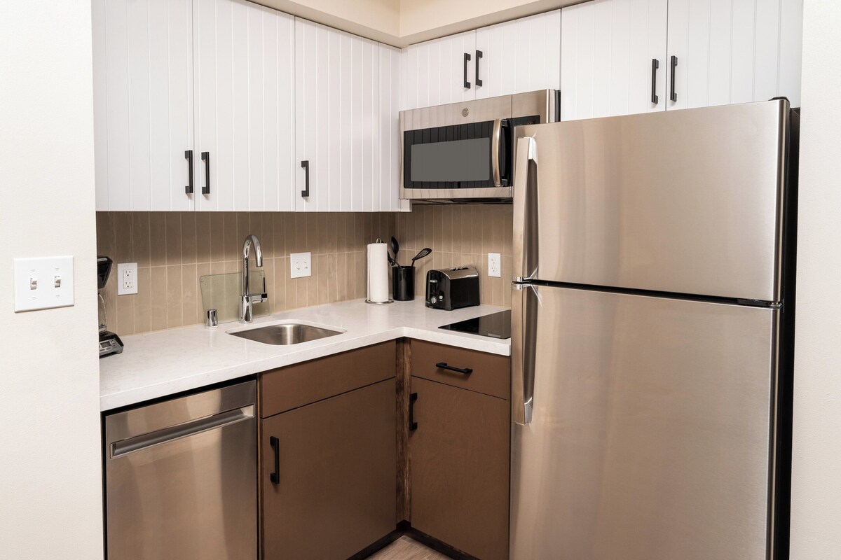 Una cocina moderna con electrodomésticos de acero inoxidable, armarios blancos y un microondas integrado.