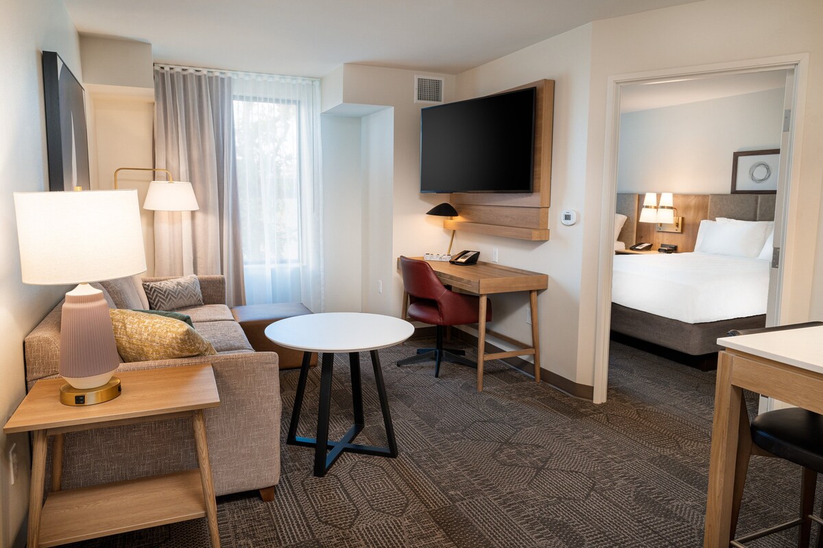 A hotel room with a sofa, a small table, a desk, a bed, a TV, and a bathroom.