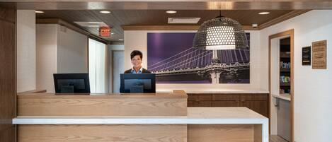A reception desk with two computer monitors, a large pendant light, and a wall-mounted exit sign.