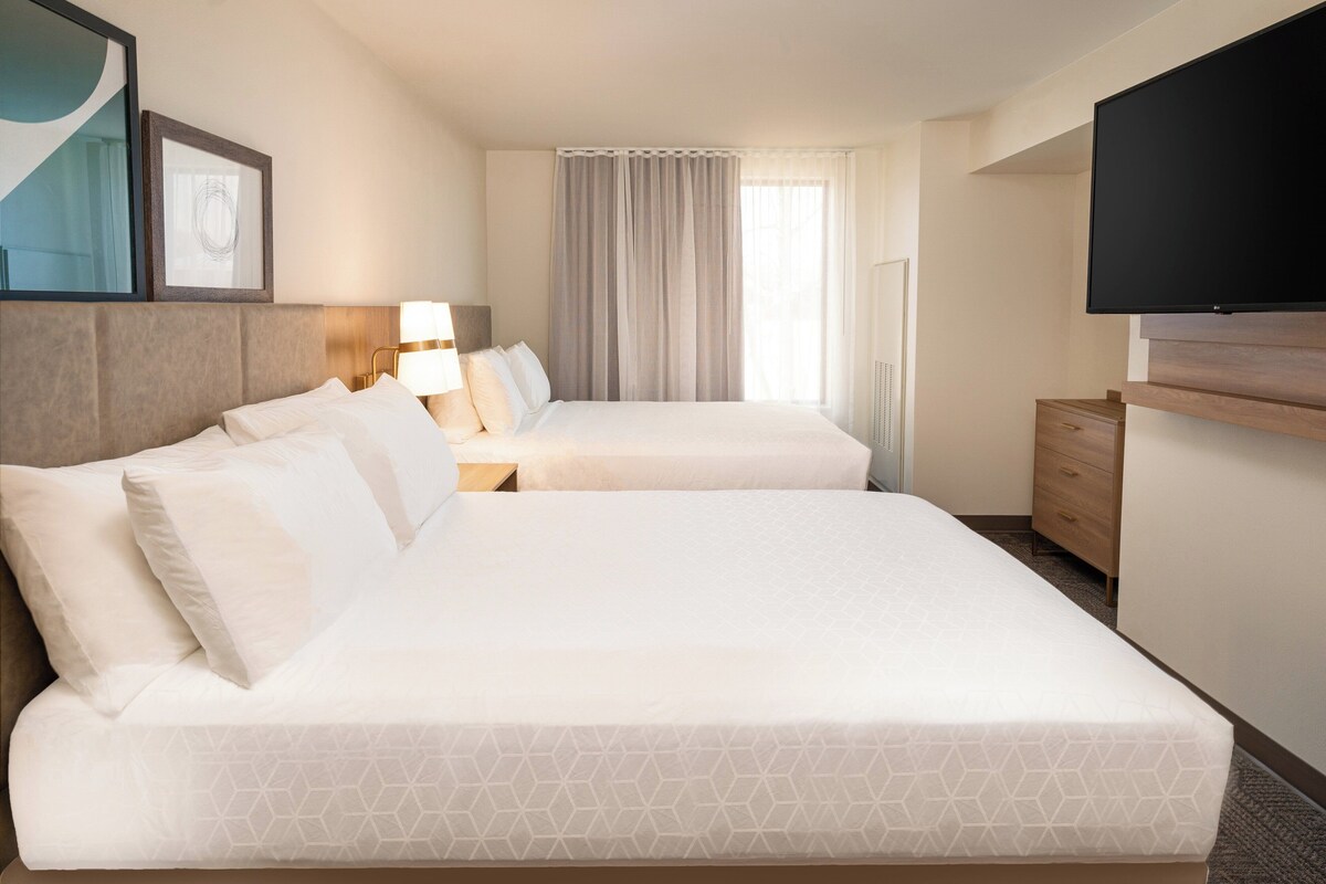 Una habitación de hotel con dos camas, televisión, escritorio y ventana con cortinas.