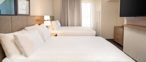Habitación de hotel con dos camas, televisión, escritorio y ventana con cortinas.