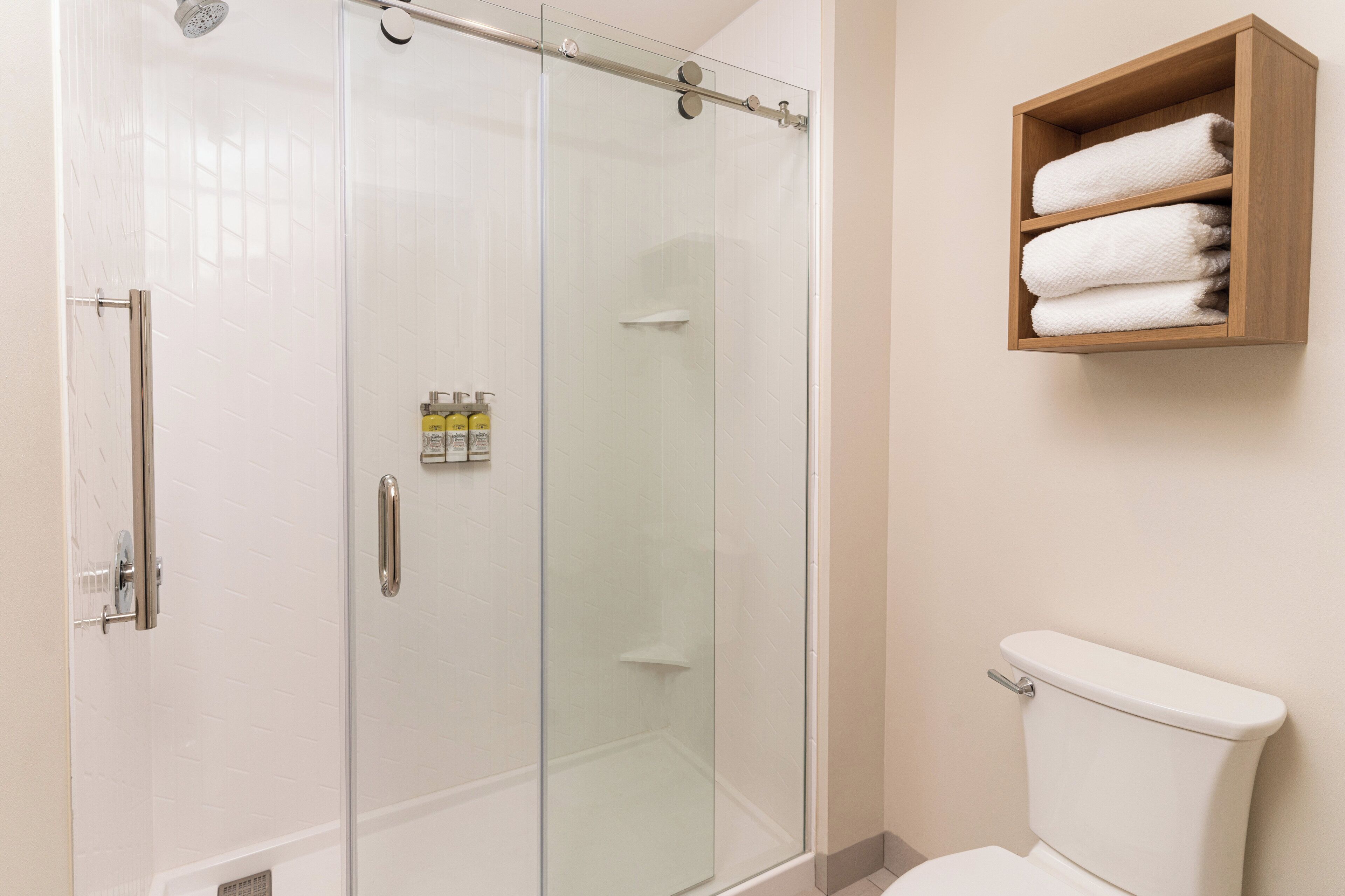 Une salle de bain avec une douche à parois de verre, des toilettes et une étagère en bois où sont posées des serviettes.