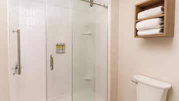 Une salle de bain avec une douche à parois de verre, des toilettes et une étagère en bois où sont posées des serviettes.