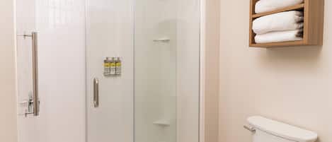 A bathroom with a glass-enclosed shower, a toilet, and a wooden shelf with towels.