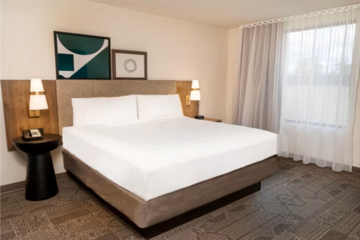 A neatly made bed with white linens, a headboard, two bedside lamps, and a small table with a lamp.