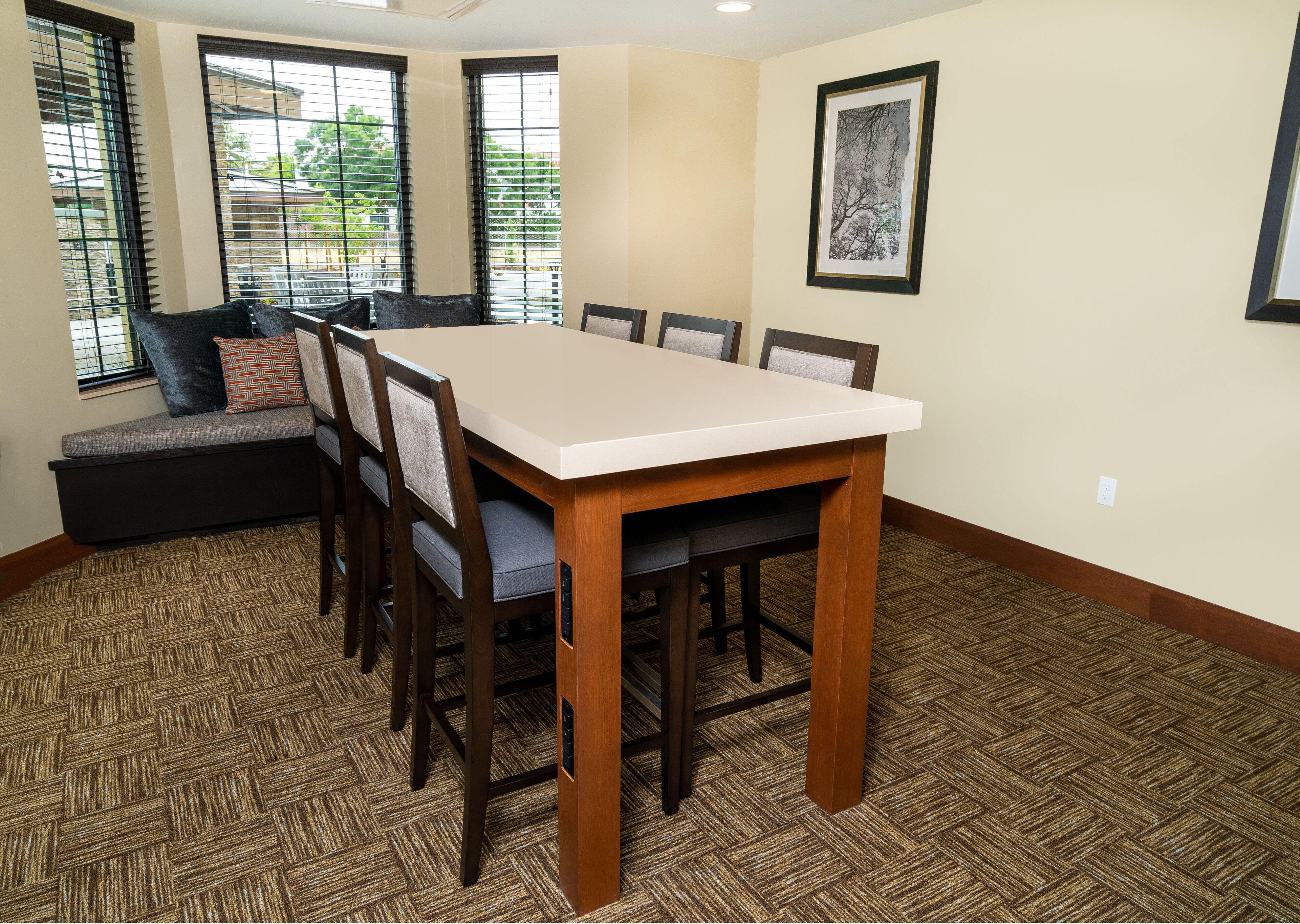 A dining area with a rectangular table, wooden chairs, a bench with cushions, and a patterned carpet.