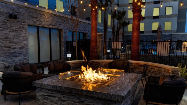 An outdoor seating area with a stone fire pit, lounge chairs, and string lights. - Staybridge Suites Temecula Wine Country by IHG (Temecula)