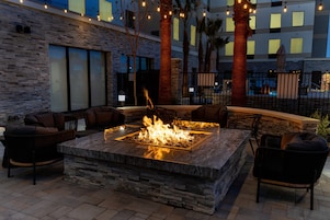 An outdoor seating area with a stone fire pit, lounge chairs, and string lights.