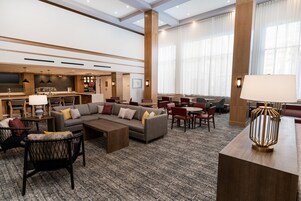 Un amplio vestíbulo de hotel con un sofá grande, zona de comedor y un bar.