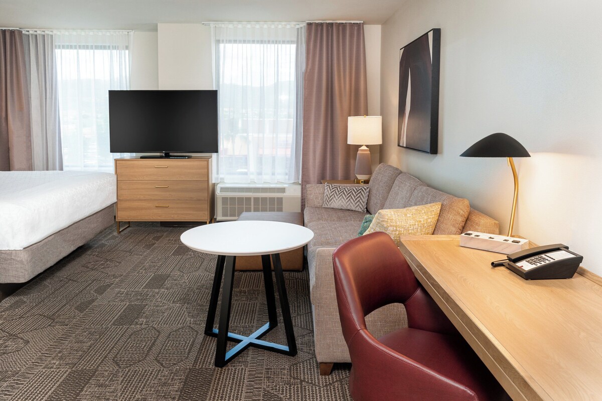 Una habitación de hotel con una cama, un sofá, un escritorio con teléfono, un televisor y una lámpara.