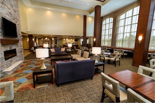 A spacious lobby with a fireplace, comfortable seating, a bar area, and large windows providing natural light.