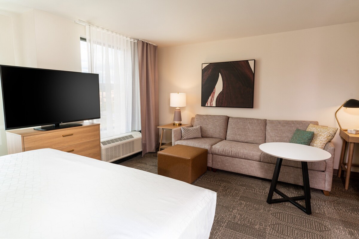 A hotel room with a bed, a sofa, a TV, a lamp, and a painting on the wall.