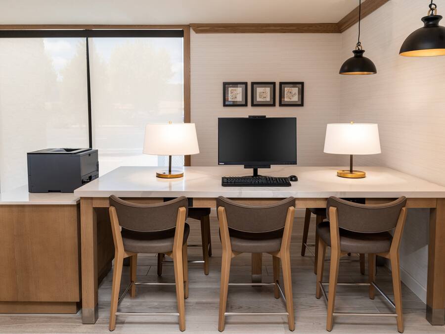 A modern kitchen with a central island, four chairs, a large flat-screen TV, two pendant lights, and framed pictures on the wall.