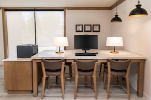 A modern kitchen with a central island, four chairs, a large flat-screen TV, two pendant lights, and framed pictures on the wall.