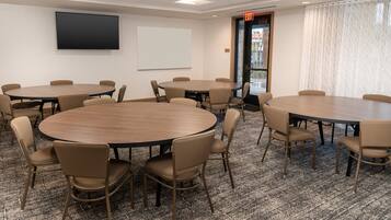 A conference room with multiple round tables and chairs, a projector screen, and an exit door.