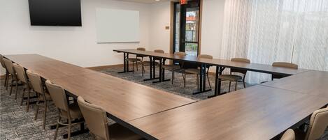 A conference room with a long table, chairs, a projector screen, and a door with an exit sign.