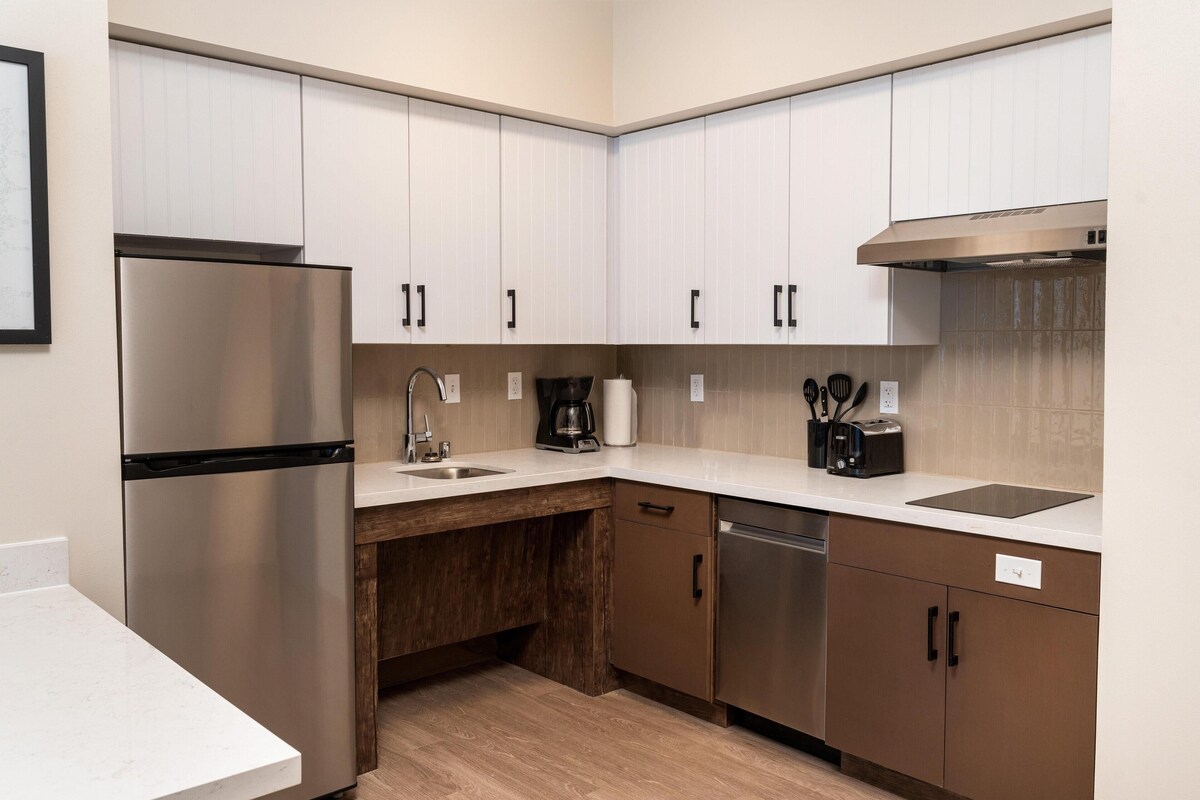 A modern kitchen with stainless steel appliances, white cabinetry, and a wooden countertop.