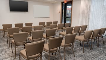Un salón de conferencias con filas de sillas color beige, una pantalla grande y una pantalla de proyección.