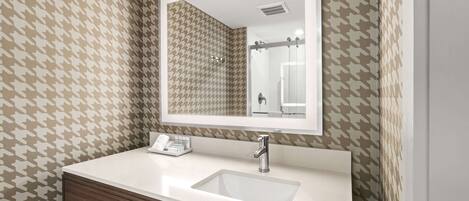 A bathroom with a white sink, a mirror, and patterned wallpaper.