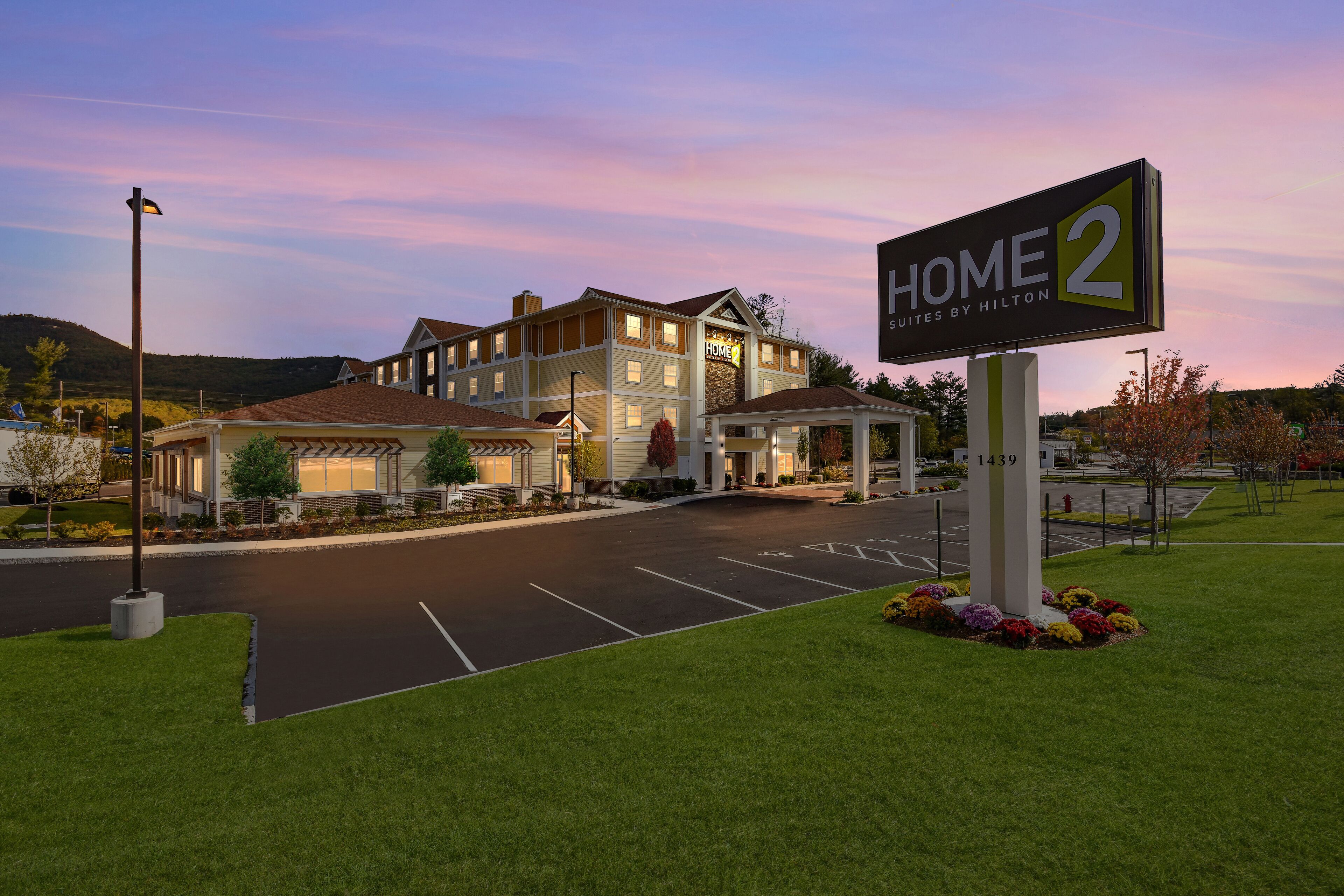 Un hotel con un letrero que dice "HOME 2 Suites by Hilton" y un estacionamiento al frente.