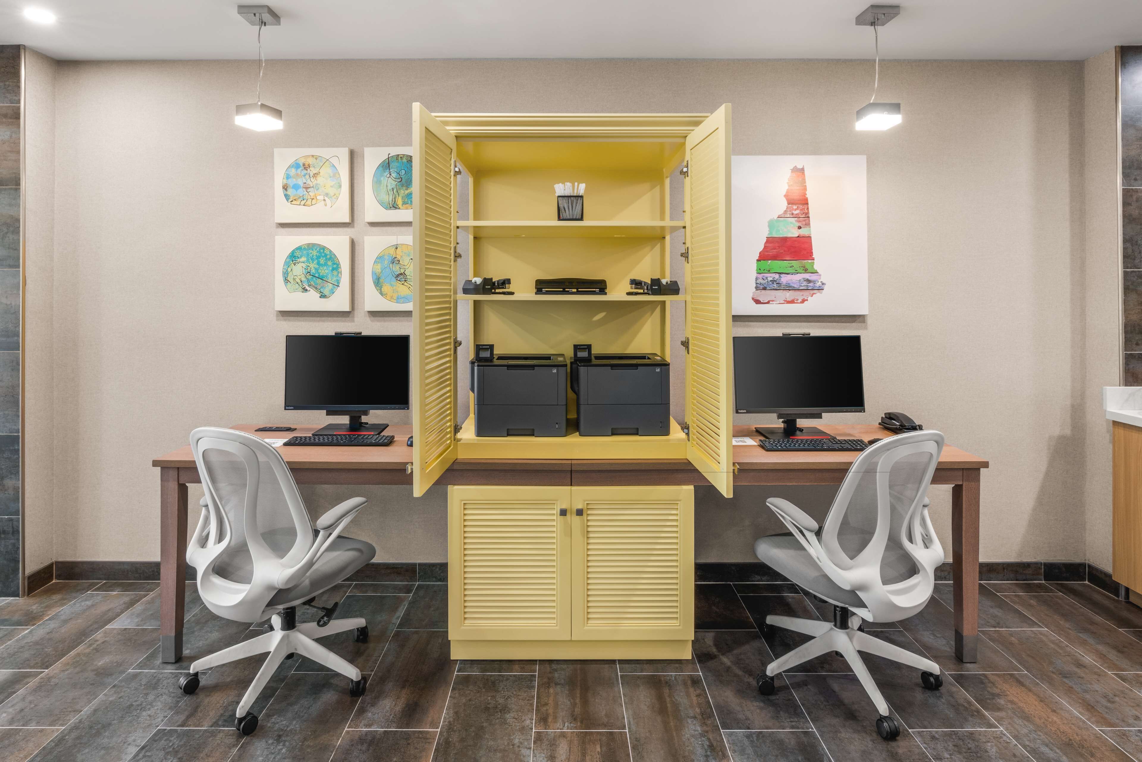 A modern office with two desks, two chairs, a yellow cabinet, and artwork on the walls.