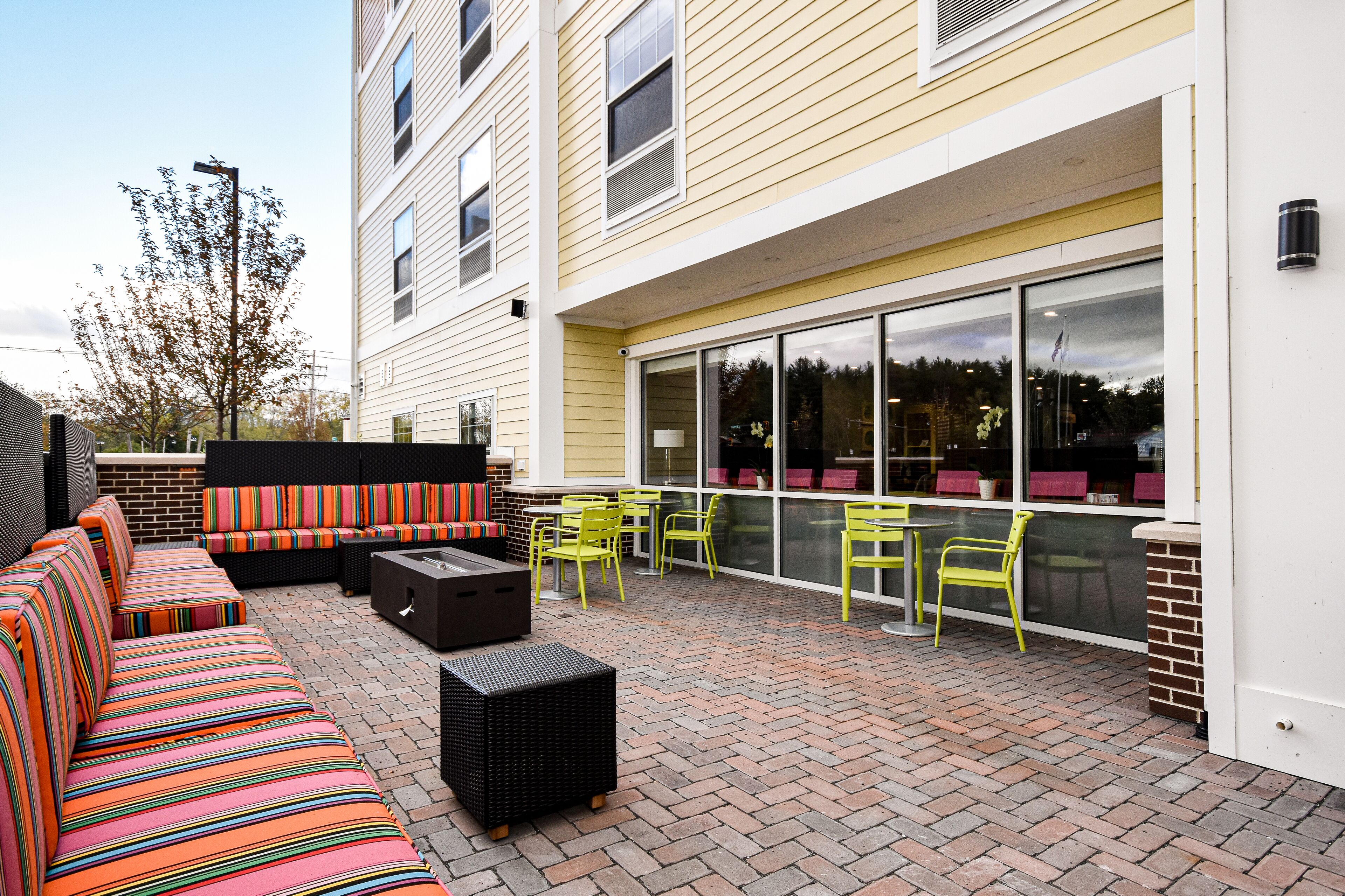 An outdoor patio with a striped sofa, yellow chairs, and a brick floor.