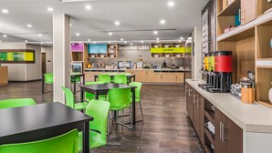 A modern cafe with green chairs and tables, a coffee machine, and a counter with a sign reading "inspired table". - Home2 Suites by Hilton North Conway (North Conway)