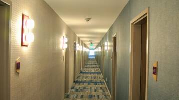 A hotel hallway with carpeted floors, light fixtures on the walls, and doors with room numbers.