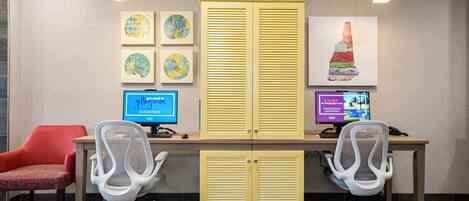 A modern office space with two desks, two office chairs, a red chair, and artwork on the wall.