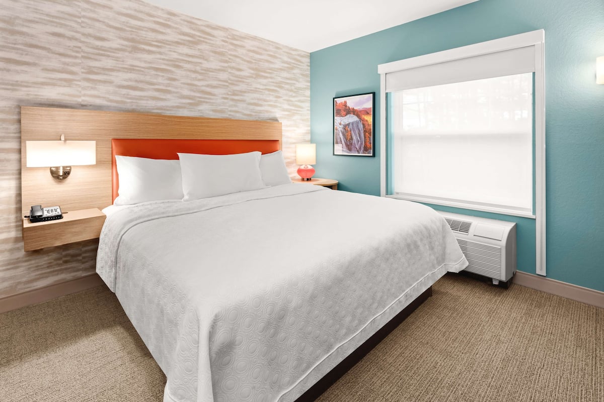 A hotel room with a bed, a nightstand, a lamp, a picture on the wall, and a window.